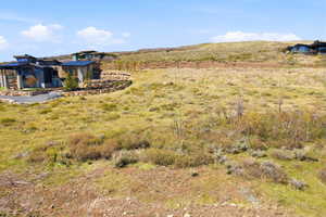 Expansive lot with natural terrain and scattered shrubs, bordered by a paved driveway and a stone retaining wall