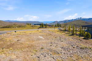 Expansive vacant lot featuring a paved road, scattered natural rock formations, and distant mountain scenery