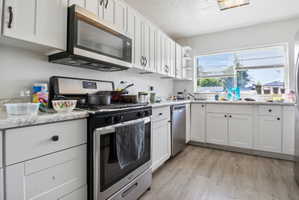 Kitchen featuring white cabinetry, light-toned countertops, wood-finish flooring, stainless steel appliances, and a window above the sink