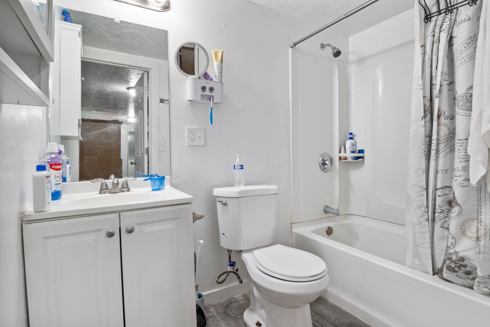 Bathroom featuring a white vanity with integrated sink, chrome faucet, wall-mounted mirror, and a full-sized bathtub with shower