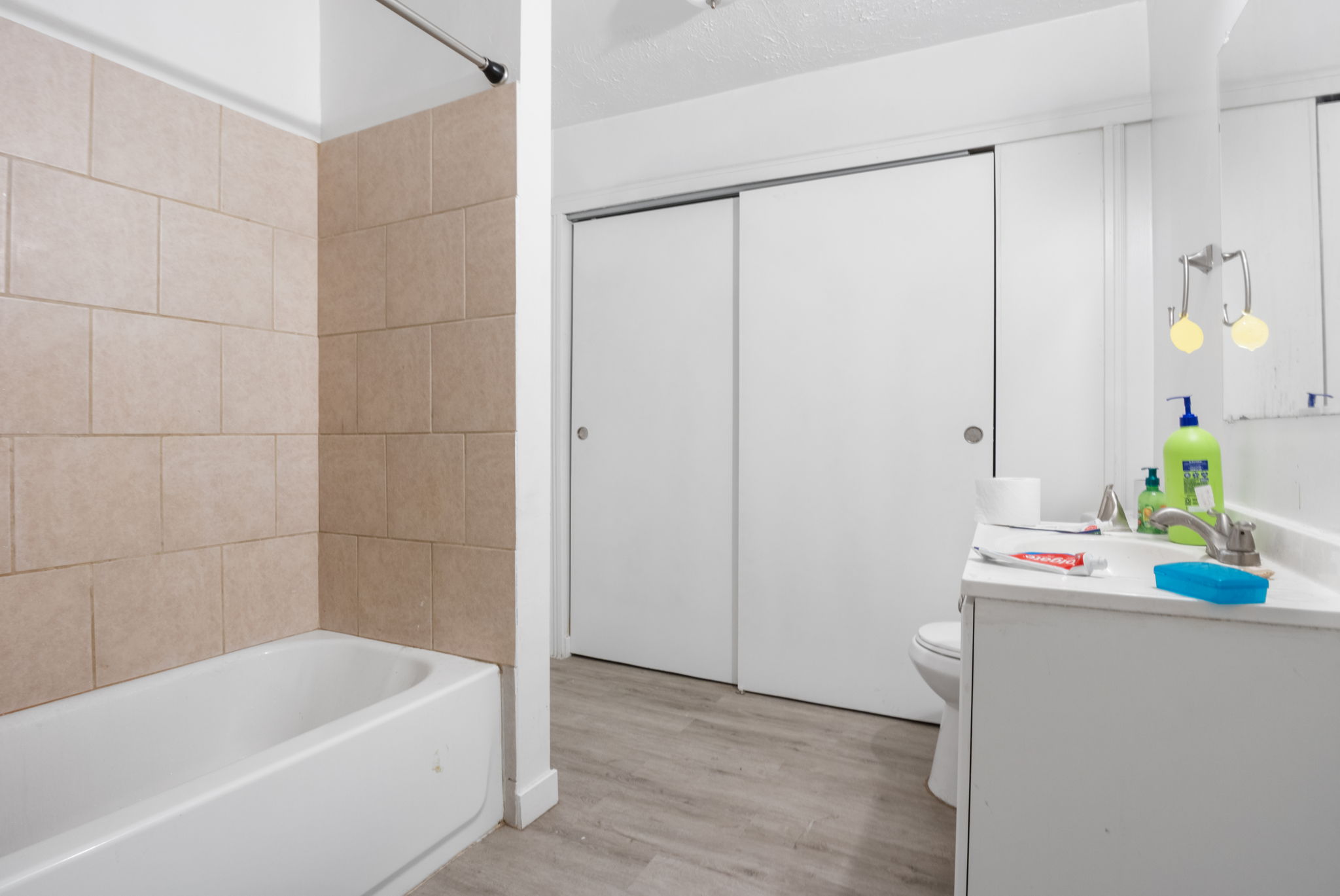 Bathroom featuring a full tub with tiled surround, a white vanity with an integrated sink, and sliding closet doors
