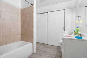 Bathroom featuring a full tub with tiled surround, a white vanity with an integrated sink, and sliding closet doors