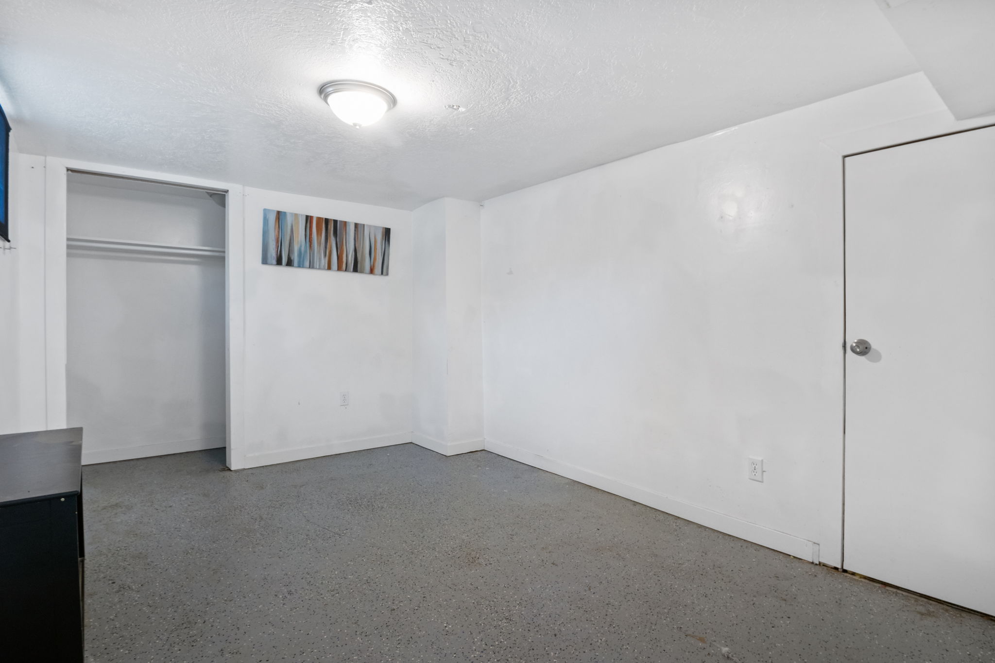 Spacious room featuring light-colored walls, a built-in closet with hanging rods, and an overhead flush-mount light fixture