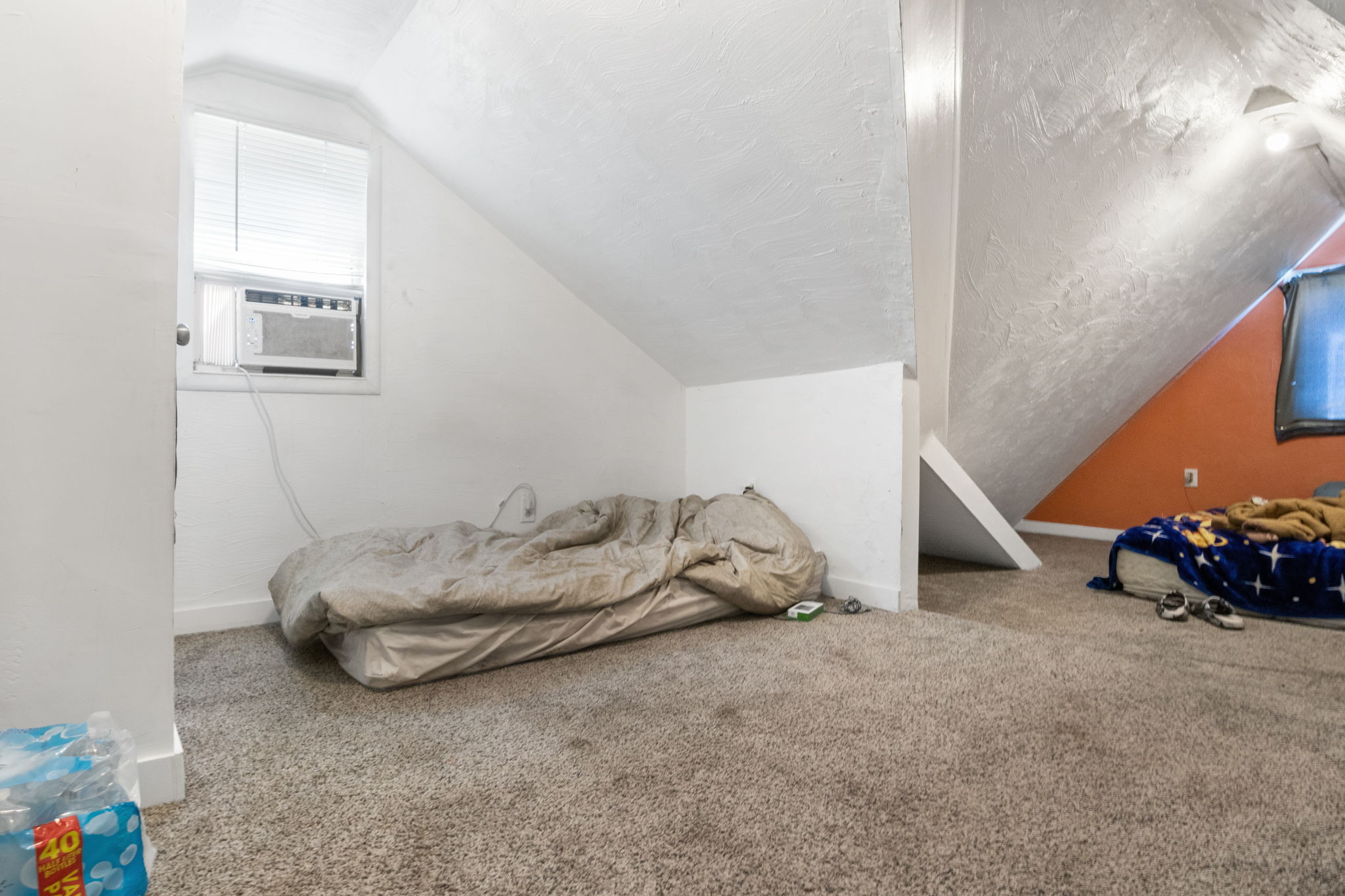 Carpeted room with sloped ceilings and a window-mounted air conditioning unit