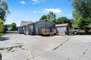 Rear exterior featuring a wooden deck with stairs, an additional access ramp, a detached storage shed, a gravel parking area, and mature trees