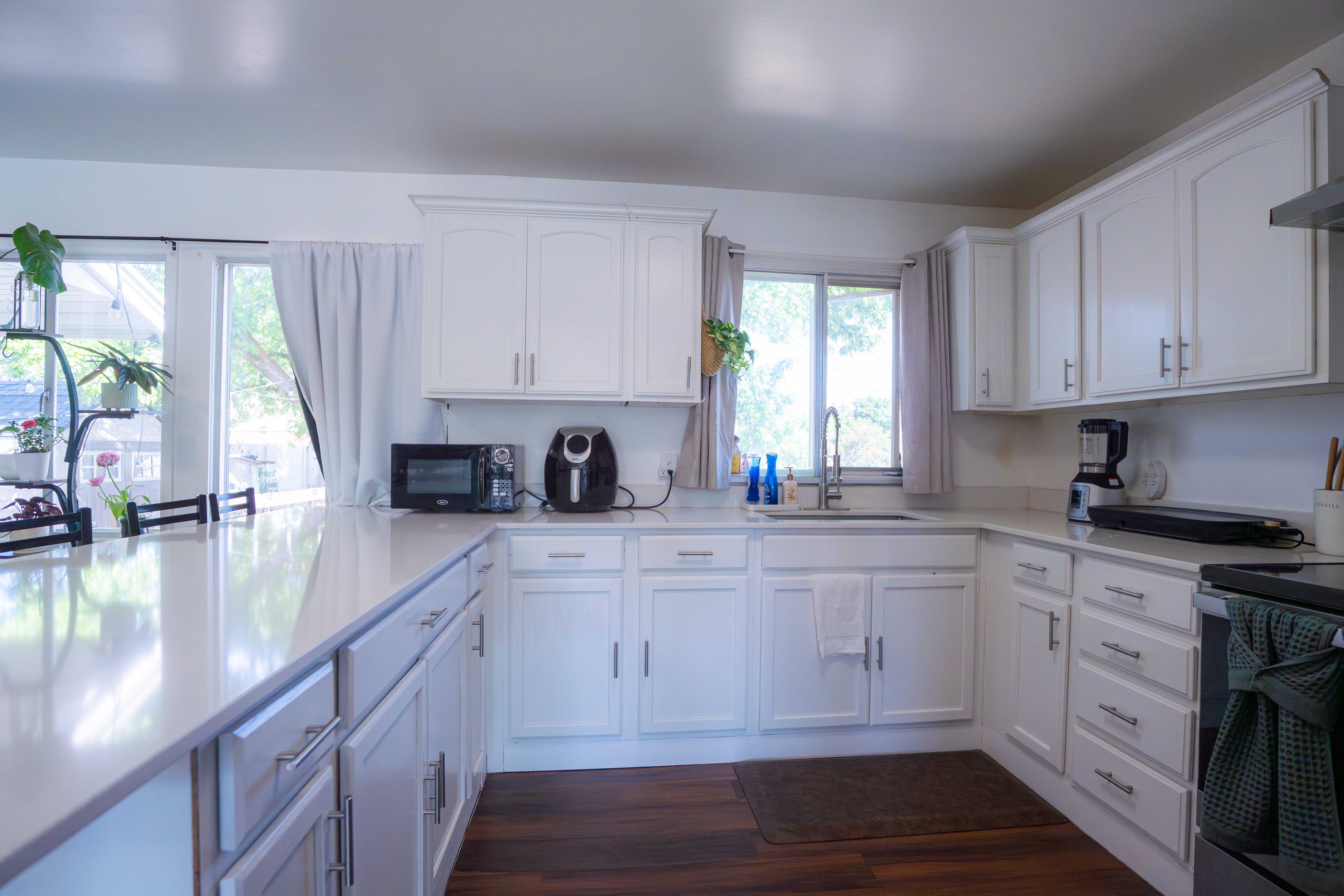 Kitchen featuring an expansive island, white cabinetry, a stainless steel sink, light-toned countertops, and wood-finish flooring