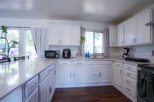 Kitchen featuring an expansive island, white cabinetry, a stainless steel sink, light-toned countertops, and wood-finish flooring
