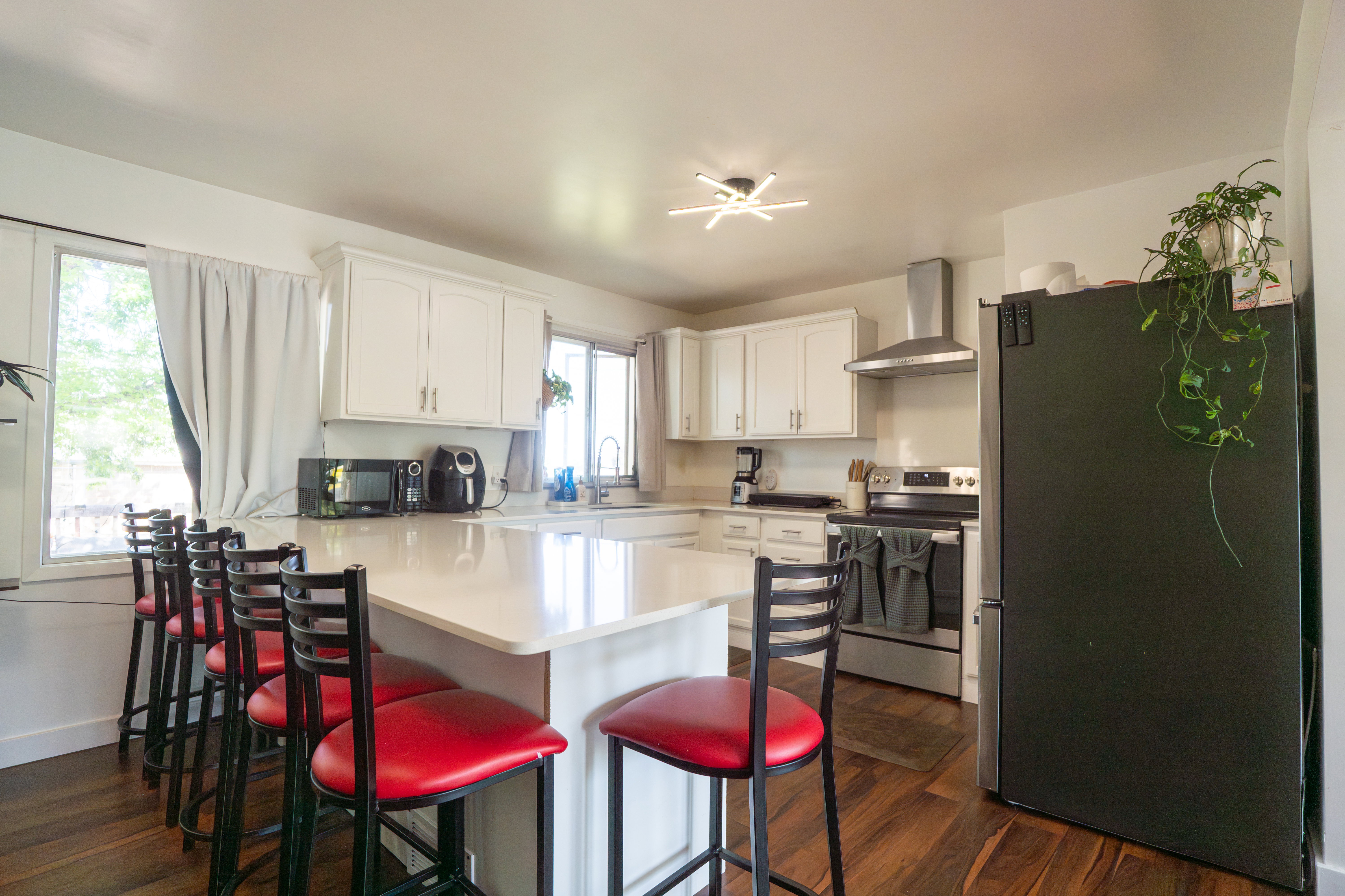 Kitchen featuring a large island with a light-toned countertop, white cabinetry, wood-finish flooring, stainless steel range with hood, and a built-in sink