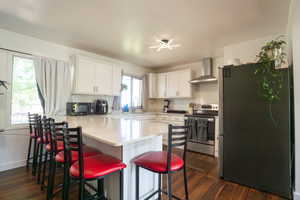 Kitchen featuring a large island with a light-toned countertop, white cabinetry, wood-finish flooring, stainless steel range with hood, and a built-in sink