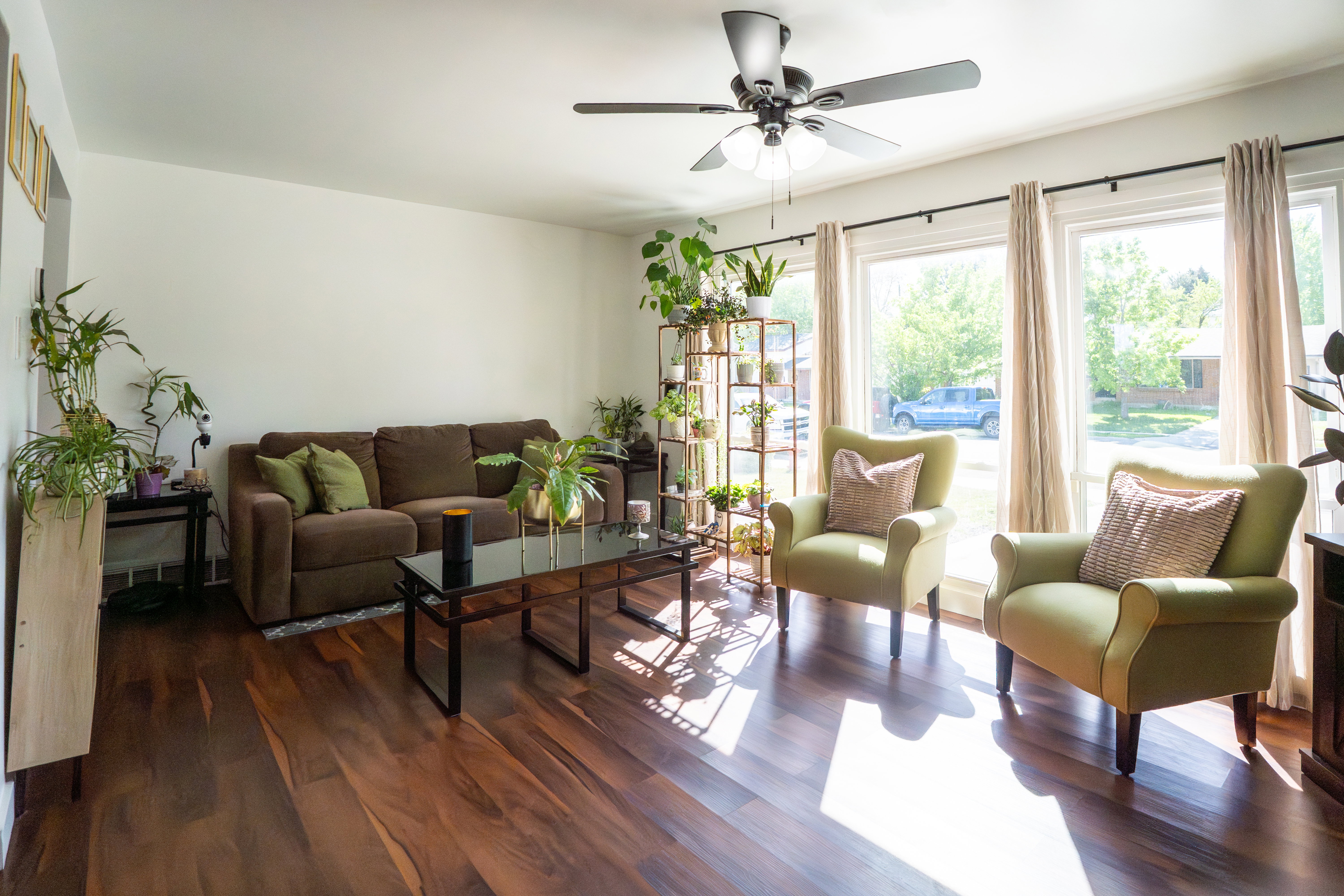Bright living area featuring wood-finish flooring, white walls, and a ceiling fan with integrated lighting