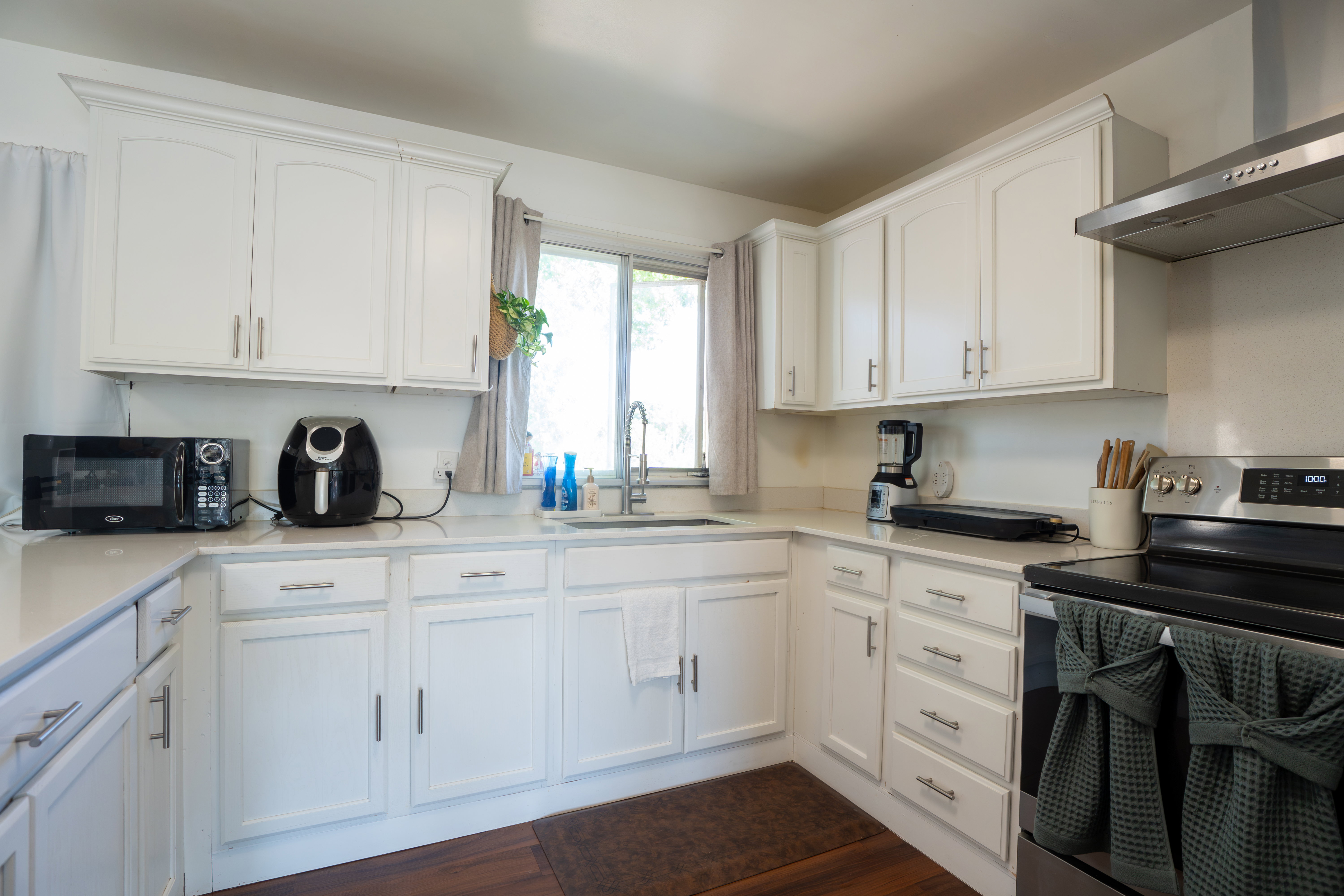 Kitchen featuring white cabinetry with brushed nickel hardware, light-toned countertops, a stainless steel sink with a gooseneck faucet, a stainless steel range with overhead ventilation, and wood-finish flooring