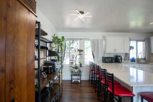 Kitchen featuring wood-finish flooring, white cabinetry, a large kitchen island with a light-toned countertop, and modern ceiling light fixtures