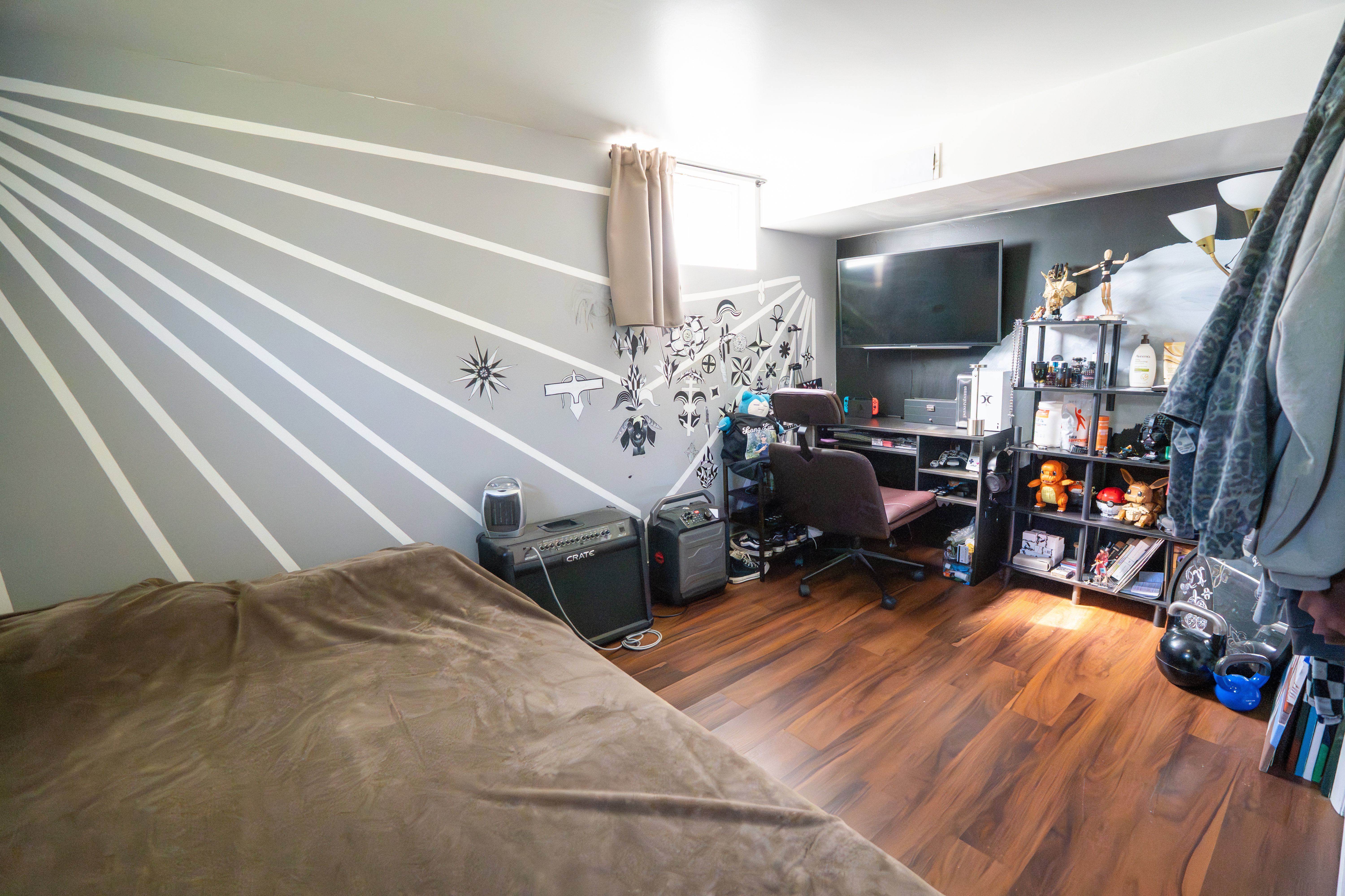 Room featuring wood-finish flooring, a decorative accent wall, a window with drapery, and a wall-mounted media console