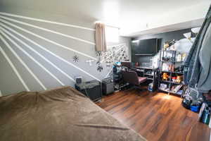 Room featuring wood-finish flooring, a decorative accent wall, a window with drapery, and a wall-mounted media console