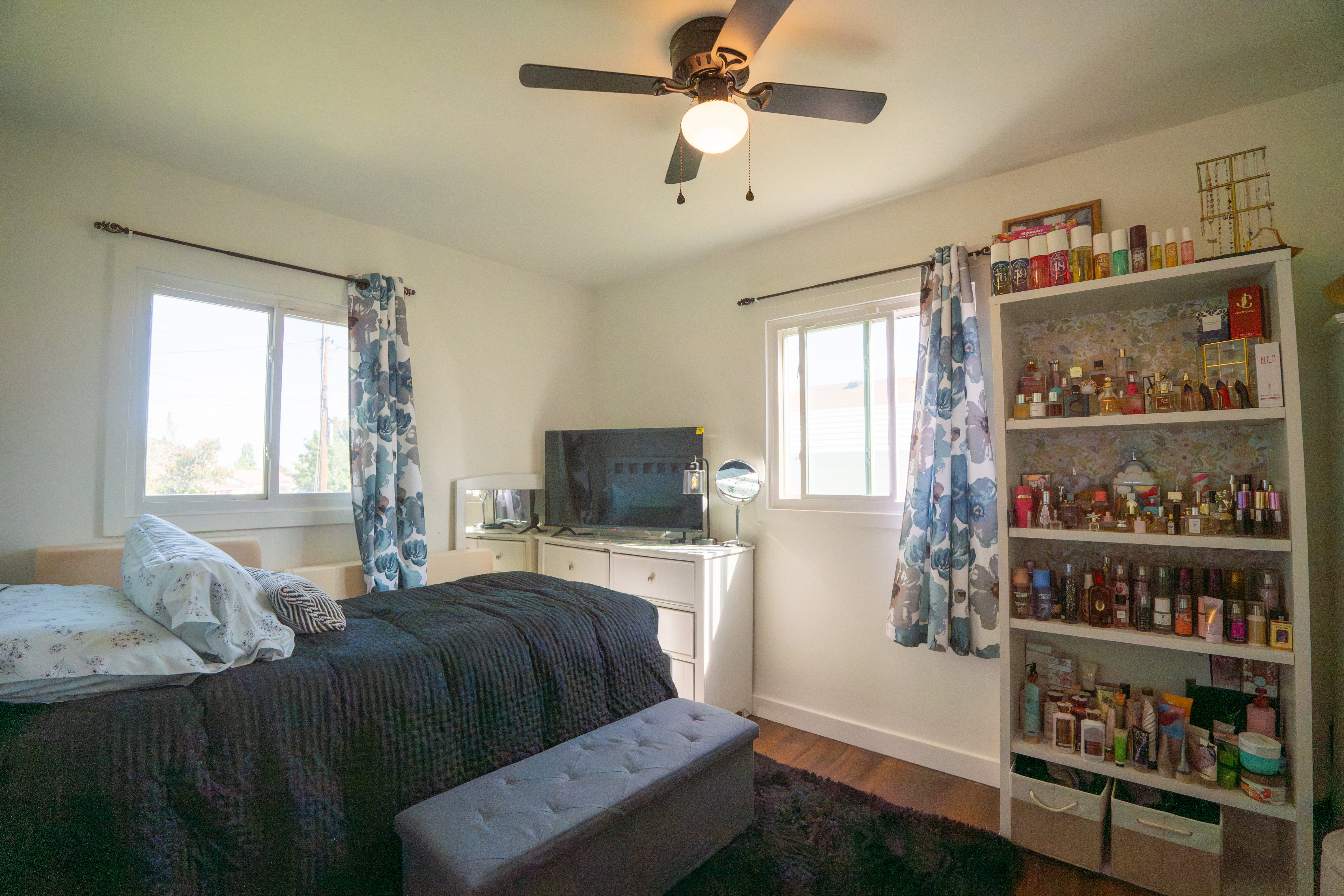 Bedroom featuring wood-finish flooring, two window openings, a ceiling fan with integrated lighting, and a built-in shelving unit