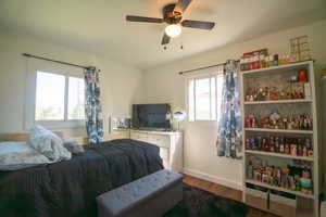 Bedroom featuring wood-finish flooring, two window openings, a ceiling fan with integrated lighting, and a built-in shelving unit