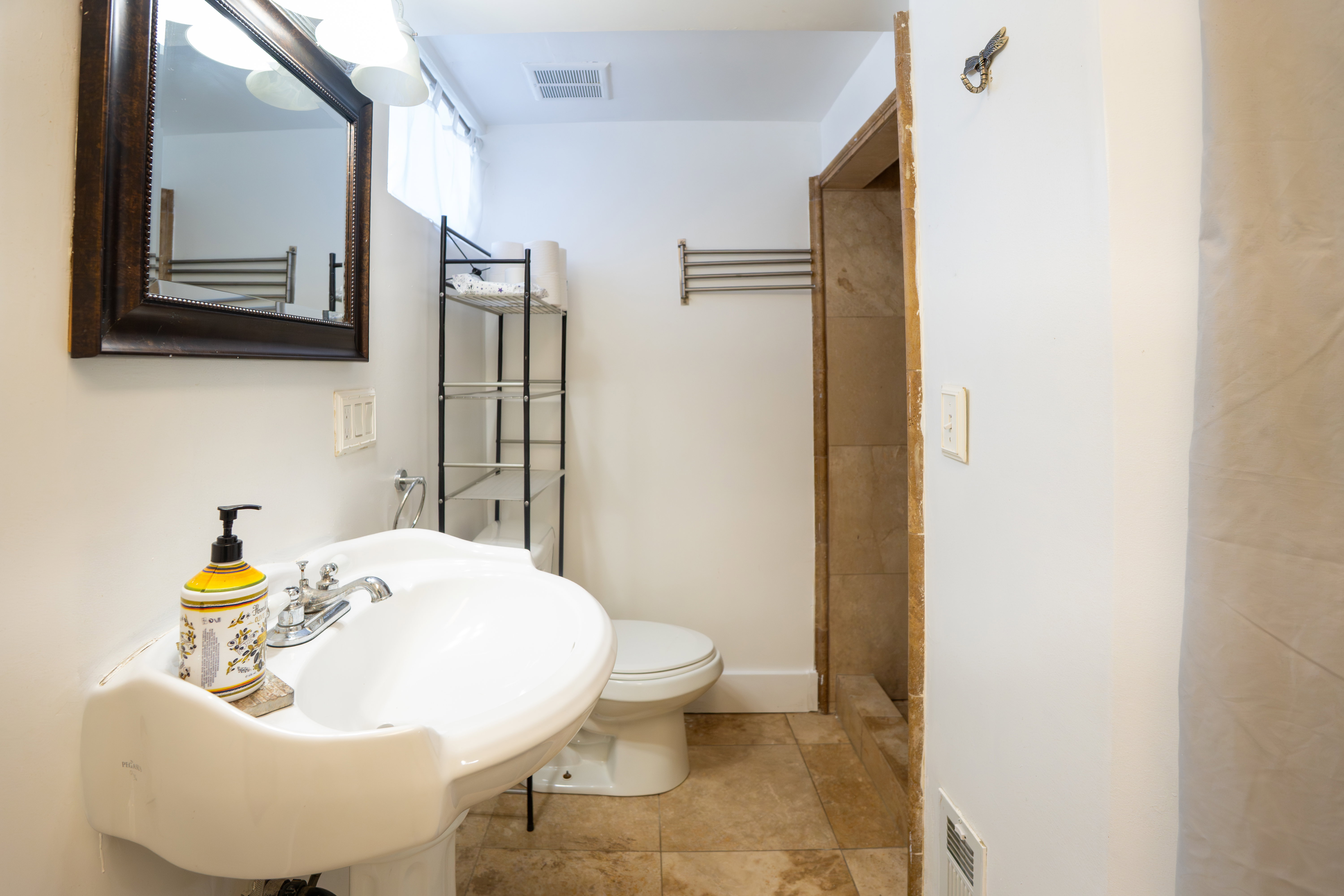 Pedestal sink with chrome fixtures, framed mirror, and tiled shower surround