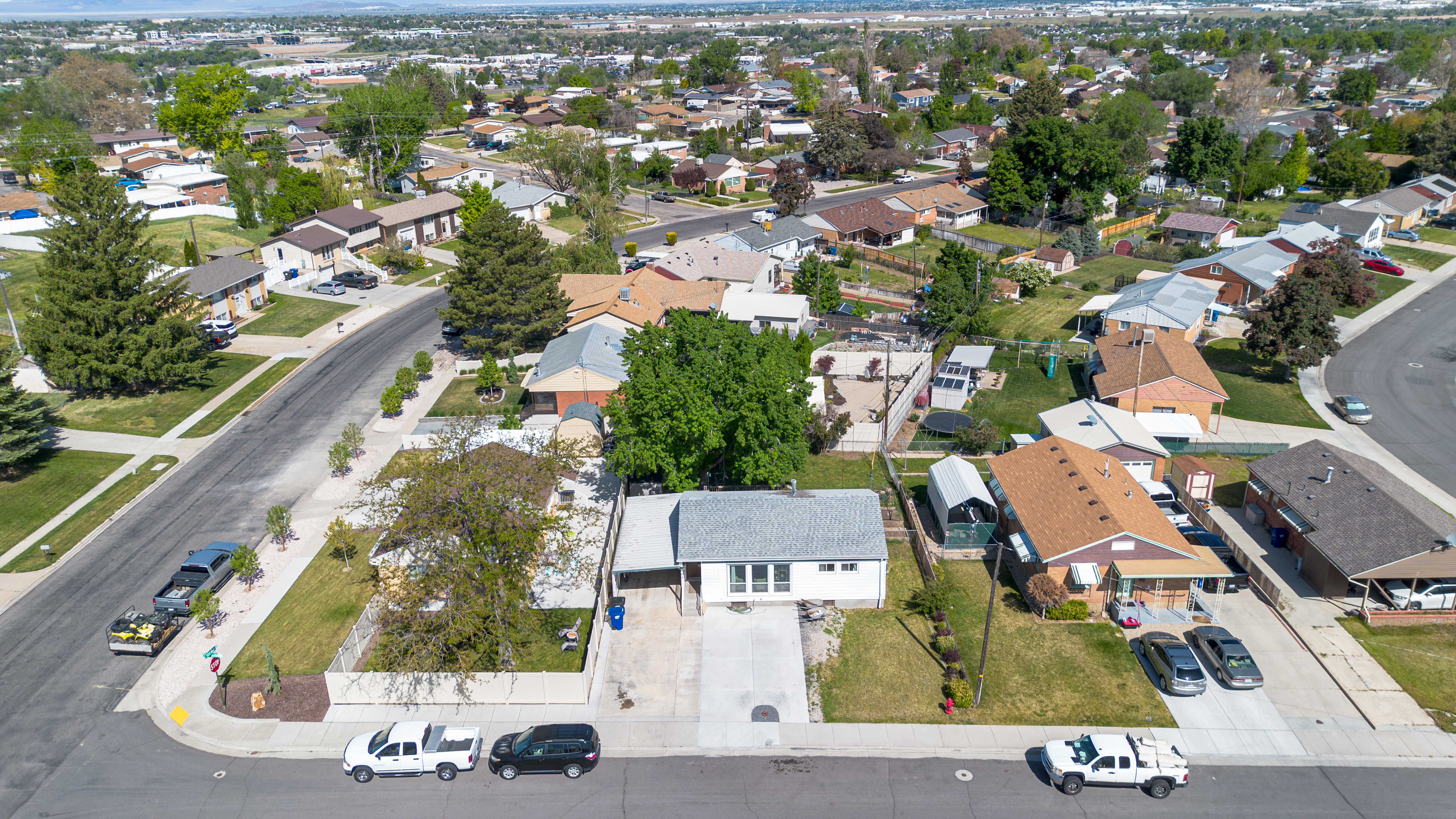 Corner lot property featuring a light-colored exterior, covered entry, and an established front yard with mature trees