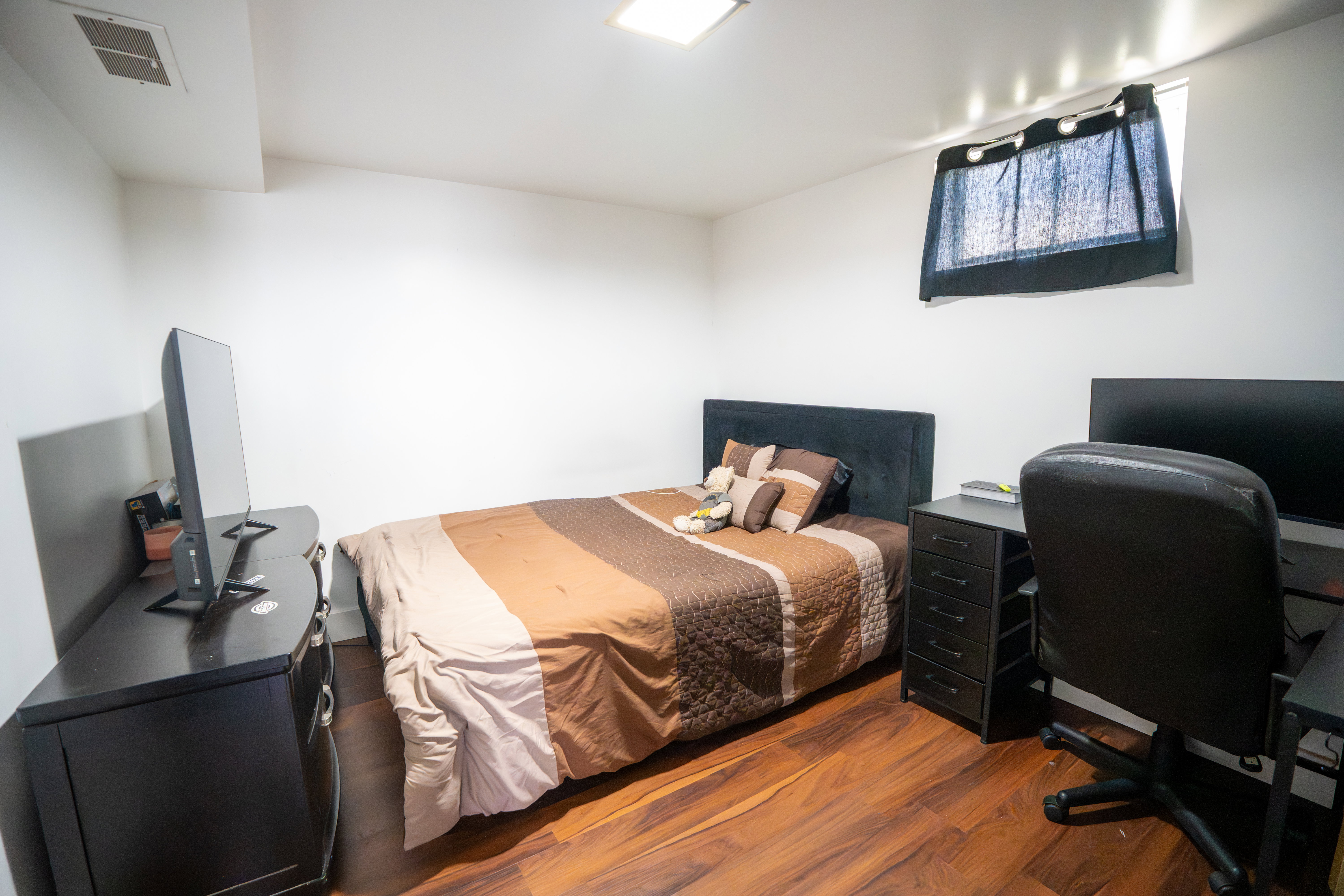 Room featuring wood-finish flooring, a rectangular ceiling light fixture, a window with dark curtains, and white painted walls