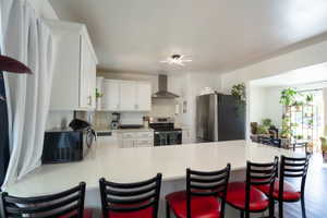 Kitchen featuring white shaker cabinetry, stainless steel appliances, a range hood, and a white countertop with an extended breakfast bar