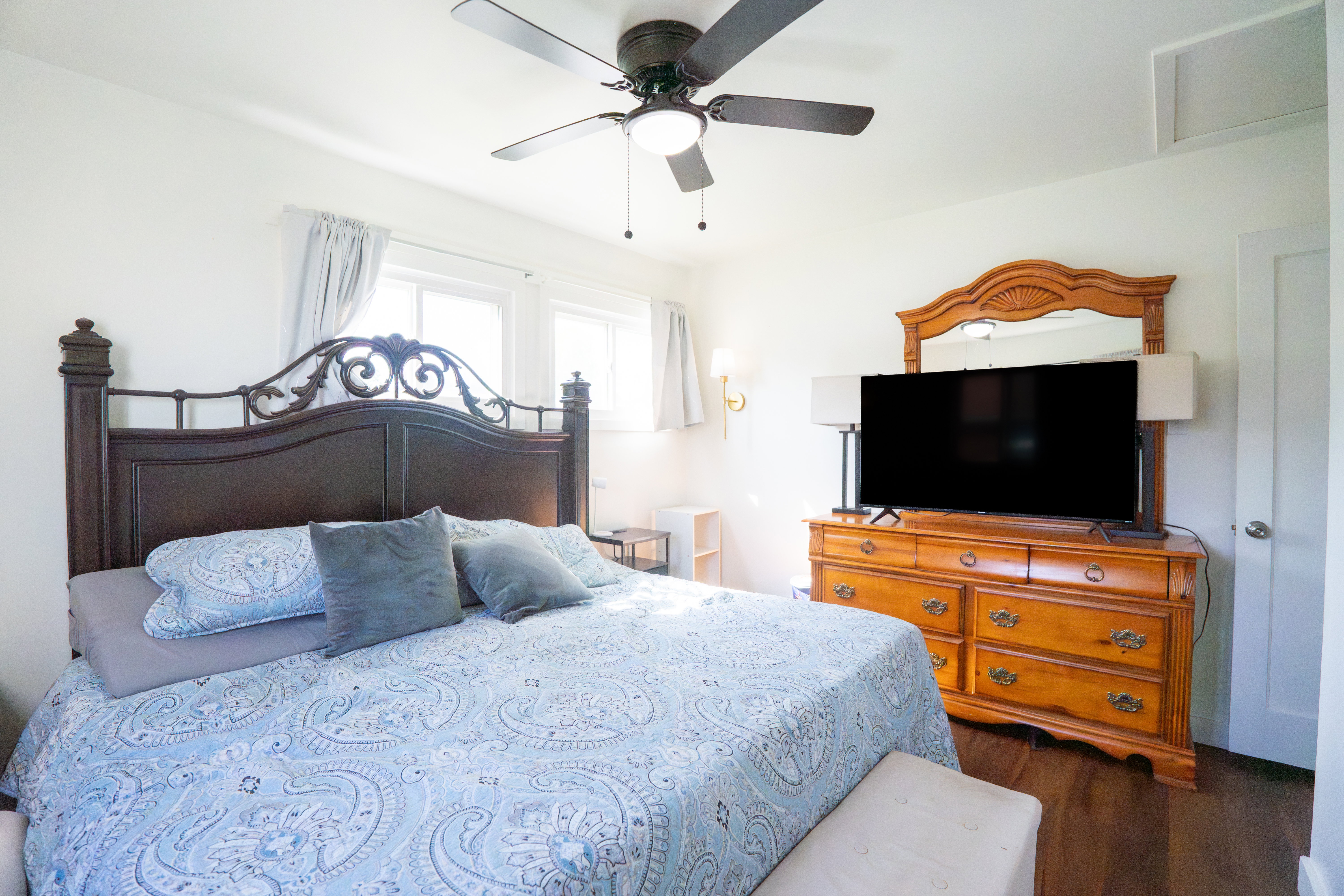 Bedroom featuring a ceiling fan with integrated lighting, multiple windows with white trim, wood-finish flooring, and a white interior door