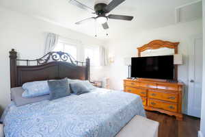 Bedroom featuring a ceiling fan with integrated lighting, multiple windows with white trim, wood-finish flooring, and a white interior door