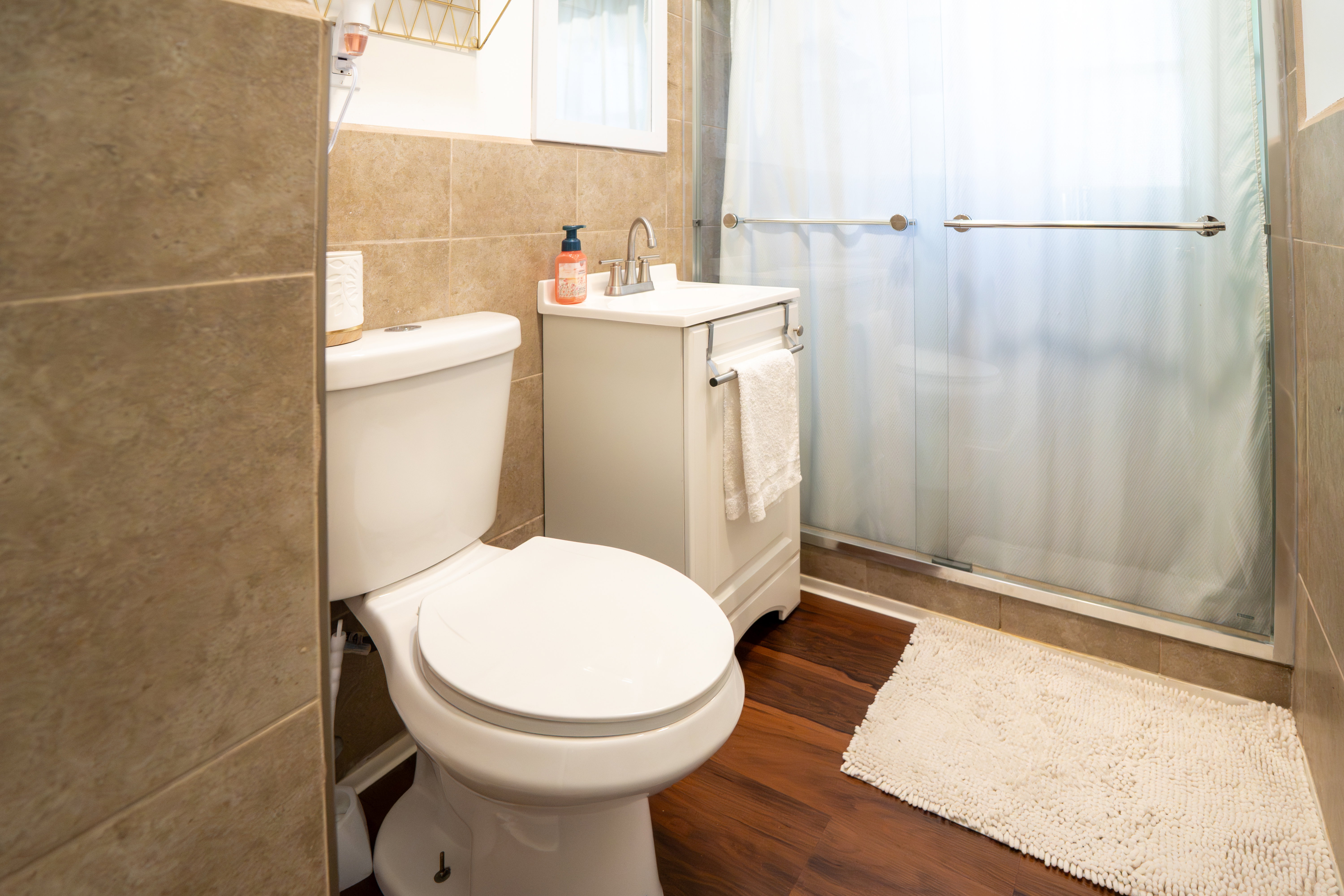Bathroom featuring wood-finish flooring, a white vanity with an integrated sink, a glass-enclosed shower, and neutral wall tiling