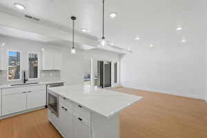 Modern kitchen featuring a white countertop island with integrated microwave, white shaker cabinetry, stainless steel dishwasher, and a gray subway tile backsplash