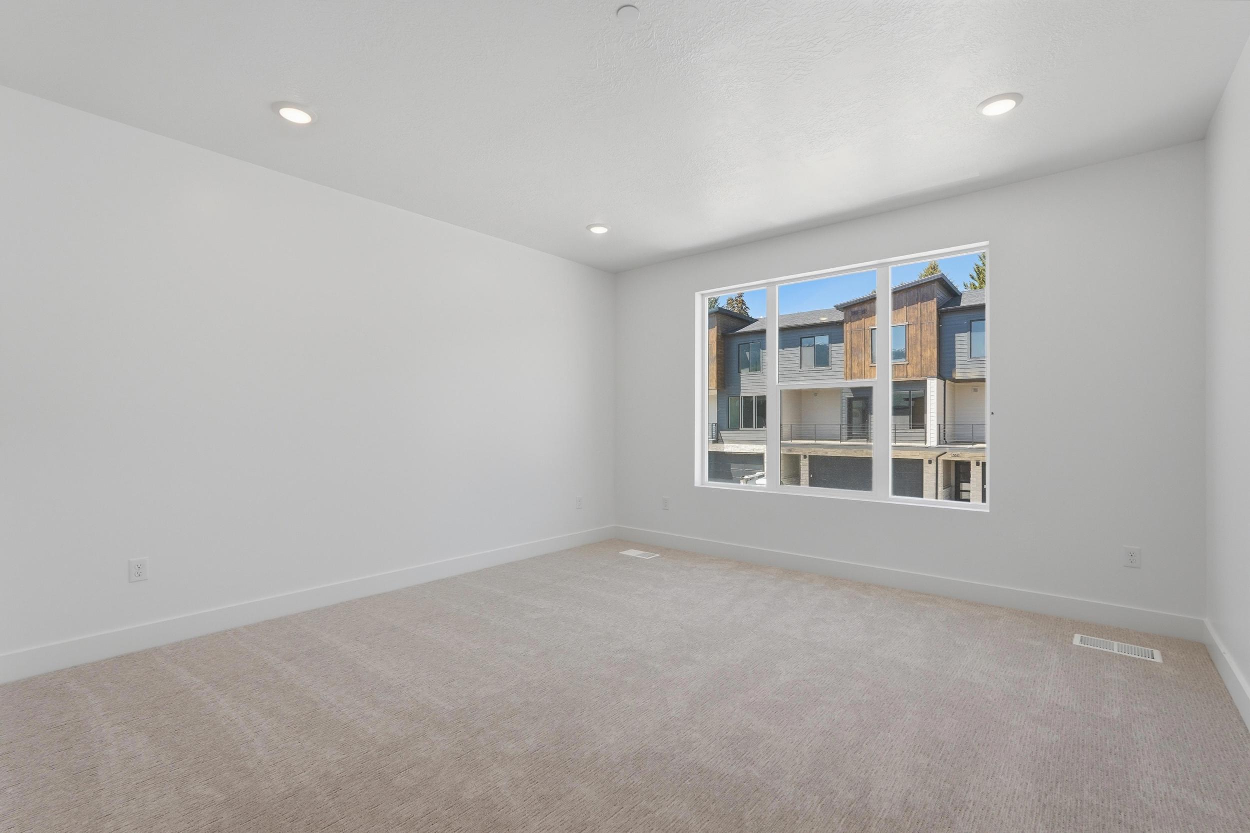 Spacious room featuring neutral carpeting, white walls, recessed ceiling lighting, and a large window