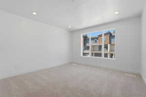 Spacious room featuring neutral carpeting, white walls, recessed ceiling lighting, and a large window