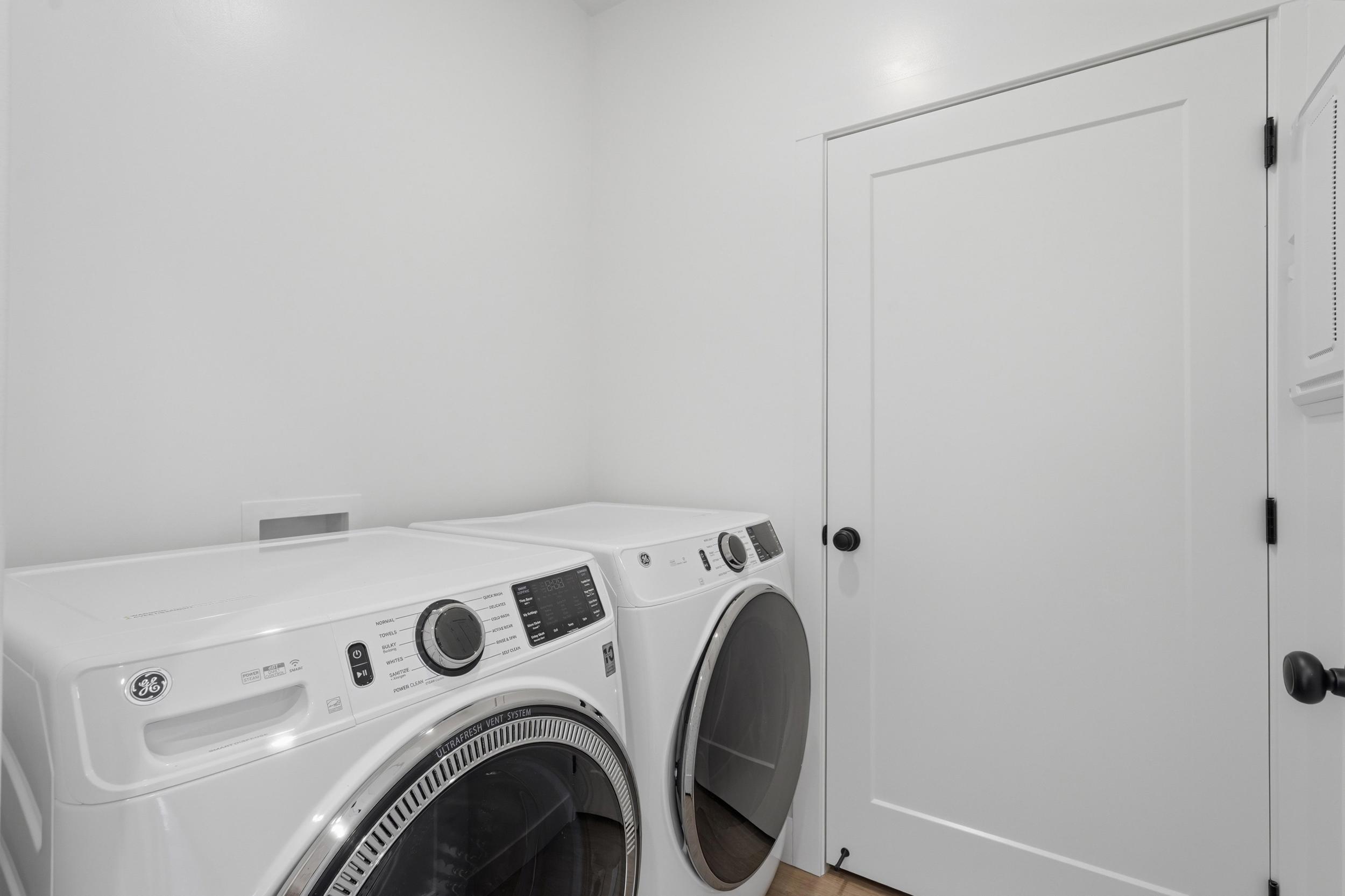 Dedicated laundry area featuring a white GE front-loading washer and dryer set, white paneled doors with black hardware, and light wood-finish flooring