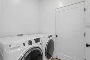 Dedicated laundry area featuring a white GE front-loading washer and dryer set, white paneled doors with black hardware, and light wood-finish flooring