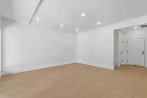 Spacious room featuring light wood-finish flooring, white walls, and recessed lighting