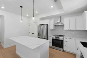 Modern kitchen with a waterfall-edge island, white shaker cabinetry, stainless steel appliances, and wood-finish flooring