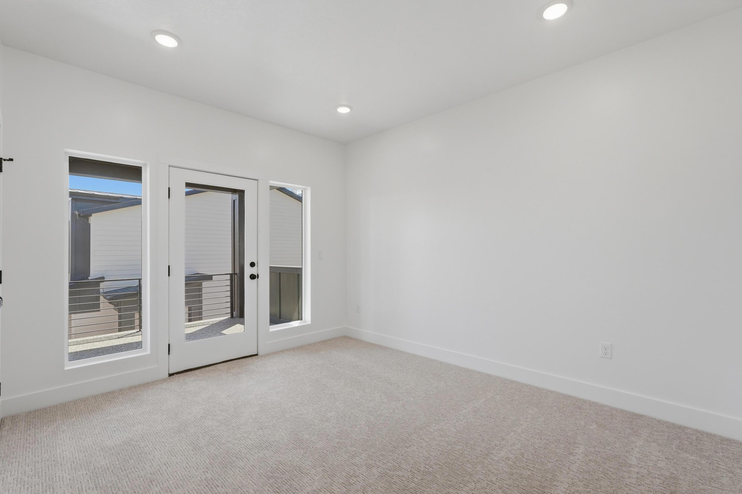 Light-filled room featuring a glass-paneled door, two fixed windows, recessed ceiling lighting, white walls, and neutral carpeting