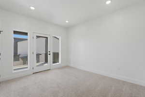 Light-filled room featuring a glass-paneled door, two fixed windows, recessed ceiling lighting, white walls, and neutral carpeting