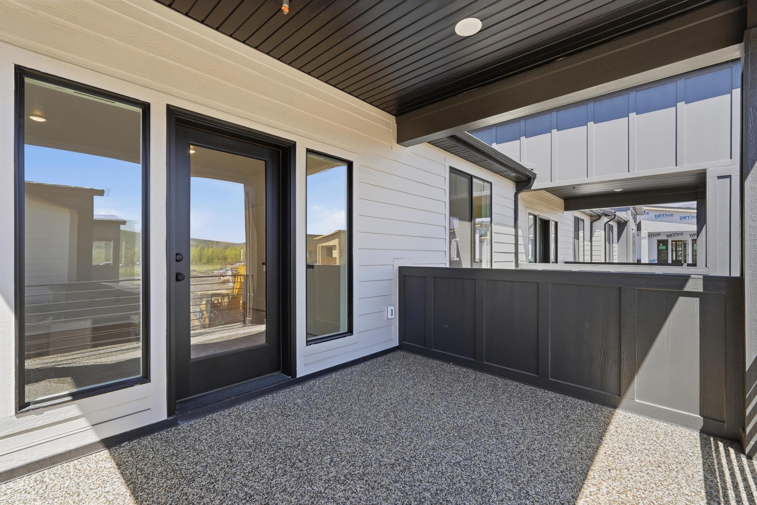 Covered patio featuring a textured aggregate surface, dark paneled privacy wall, white horizontal siding, recessed lighting, and black-framed glass door