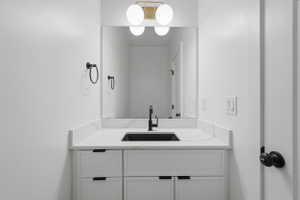 Modern vanity with a sleek black sink, white countertop, white cabinetry with black hardware, and an overhead gold-finish light fixture