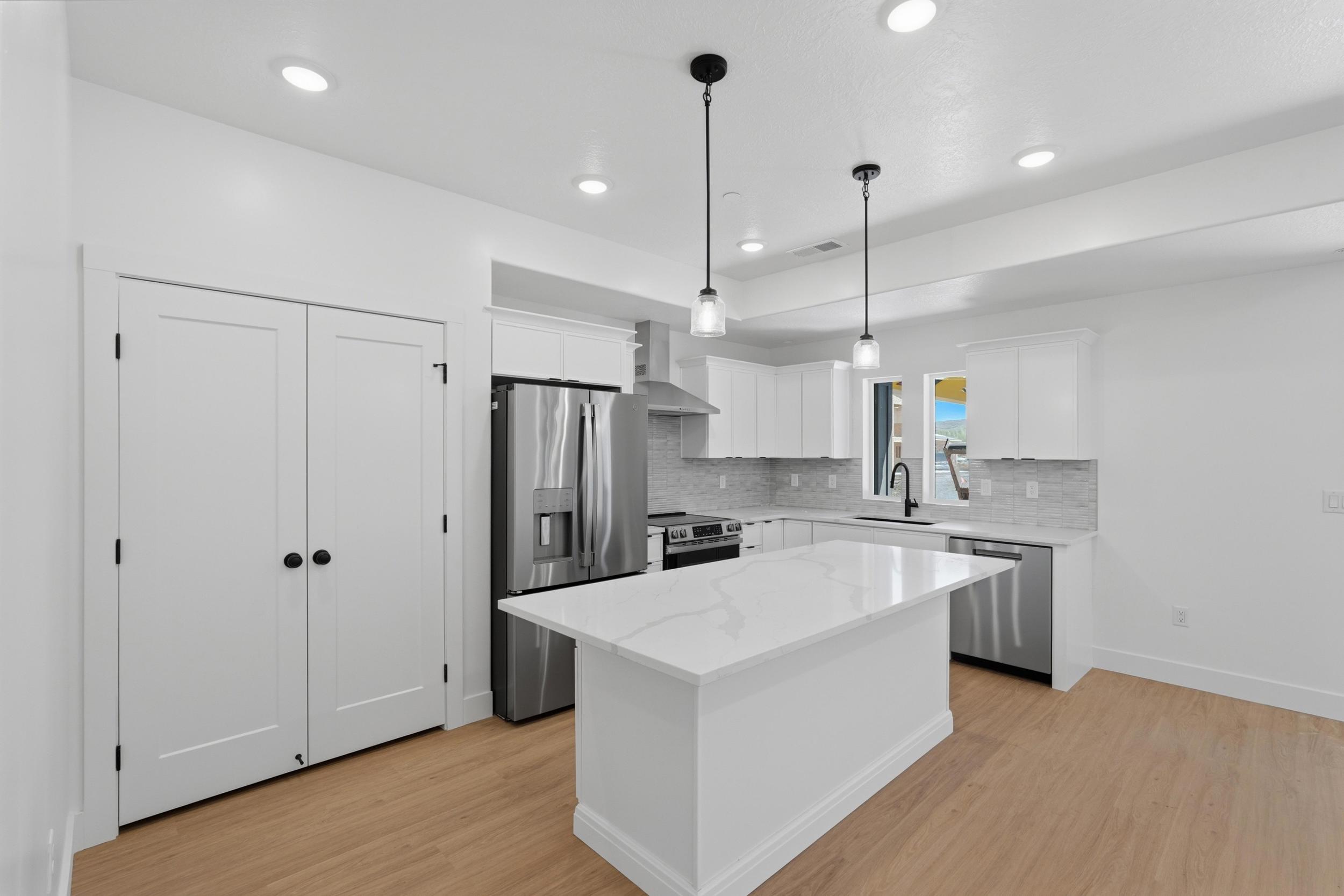 White kitchen featuring a large island with a substantial countertop, stainless steel appliances, white cabinetry, recessed lighting, and wood-finish flooring