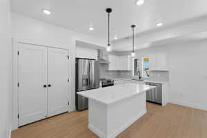 White kitchen featuring a large island with a substantial countertop, stainless steel appliances, white cabinetry, recessed lighting, and wood-finish flooring