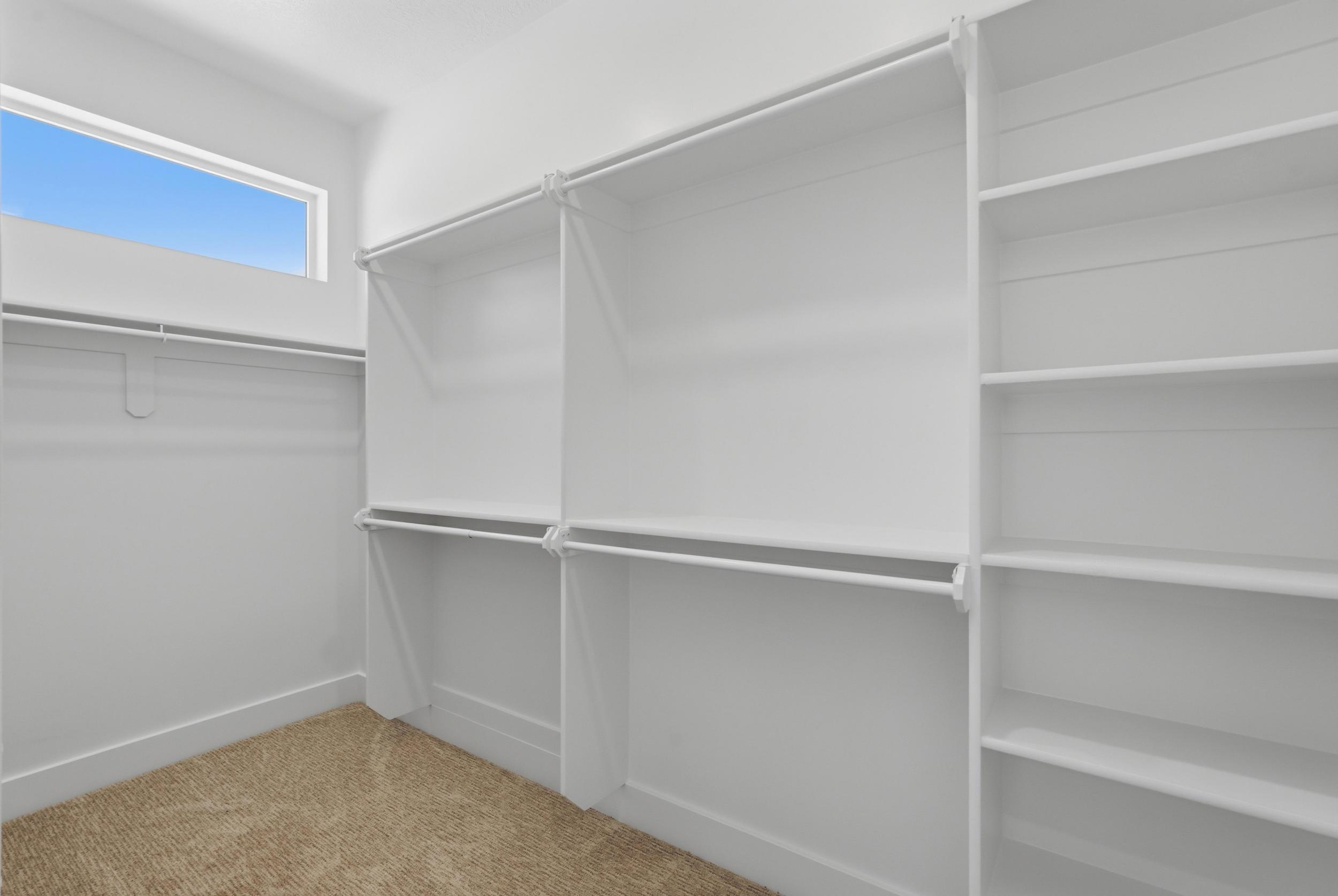 Spacious walk-in closet featuring built-in white shelving, multiple hanging rods, and a high horizontal window