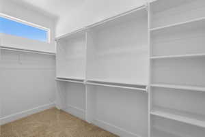 Spacious walk-in closet featuring built-in white shelving, multiple hanging rods, and a high horizontal window