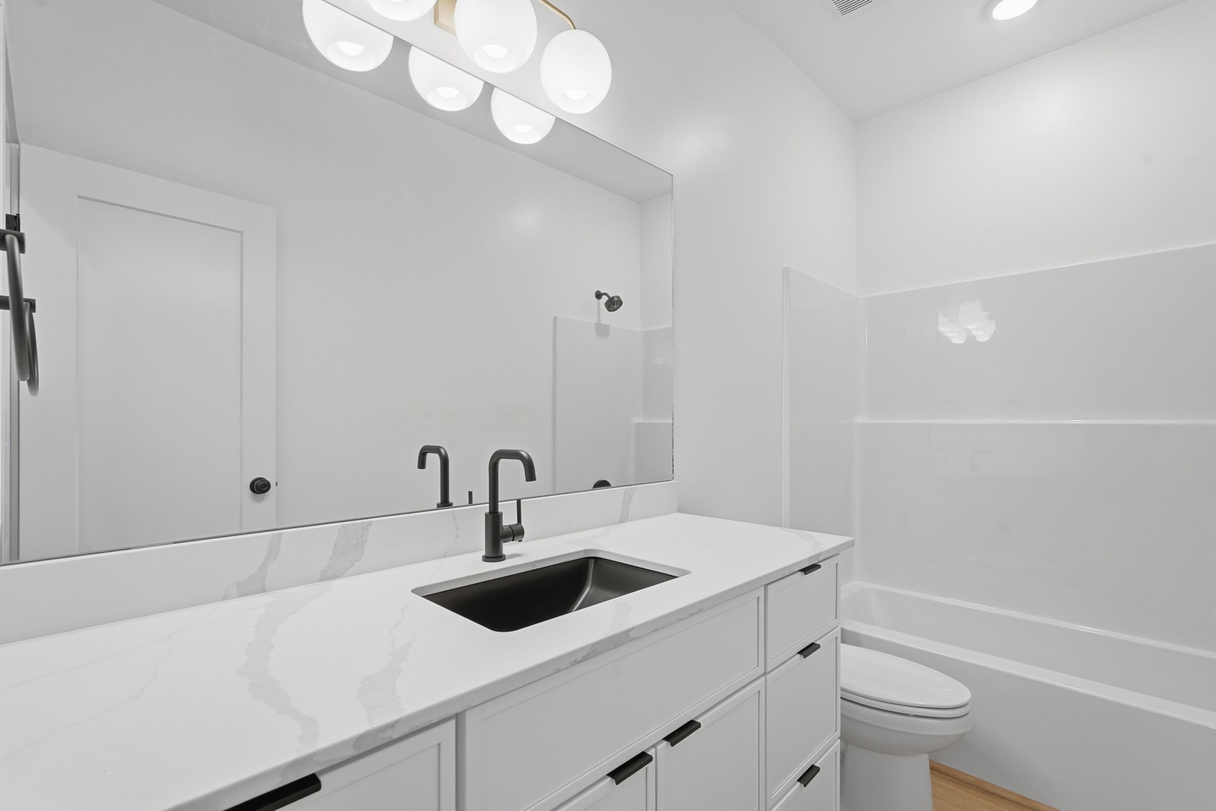 Contemporary bathroom vanity featuring a wide mirror, white countertop, and dark-finish fixtures