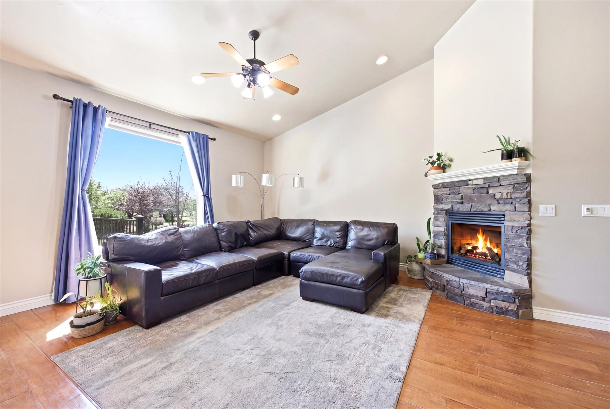 Vaulted ceiling living space featuring wood-finish flooring and a corner stone-front fireplace with a white mantel