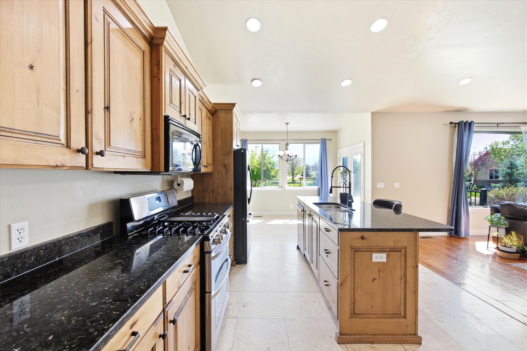 Kitchen featuring wood cabinetry, black countertops, stainless steel appliances, and an island with a built-in sink and faucet