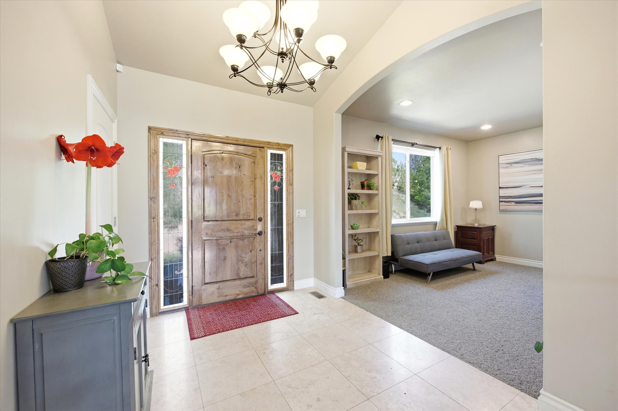 Spacious entryway featuring light-toned tile flooring, a rustic wood-finish entry door with clear glass sidelights, and a wrought iron chandelier
