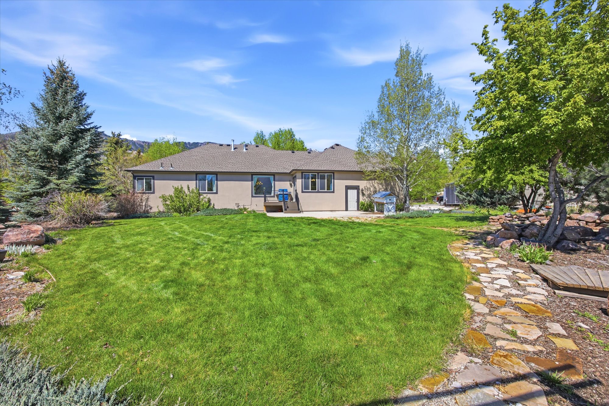 Expansive green lawn with a flagstone pathway, mature trees, and natural rock landscaping
