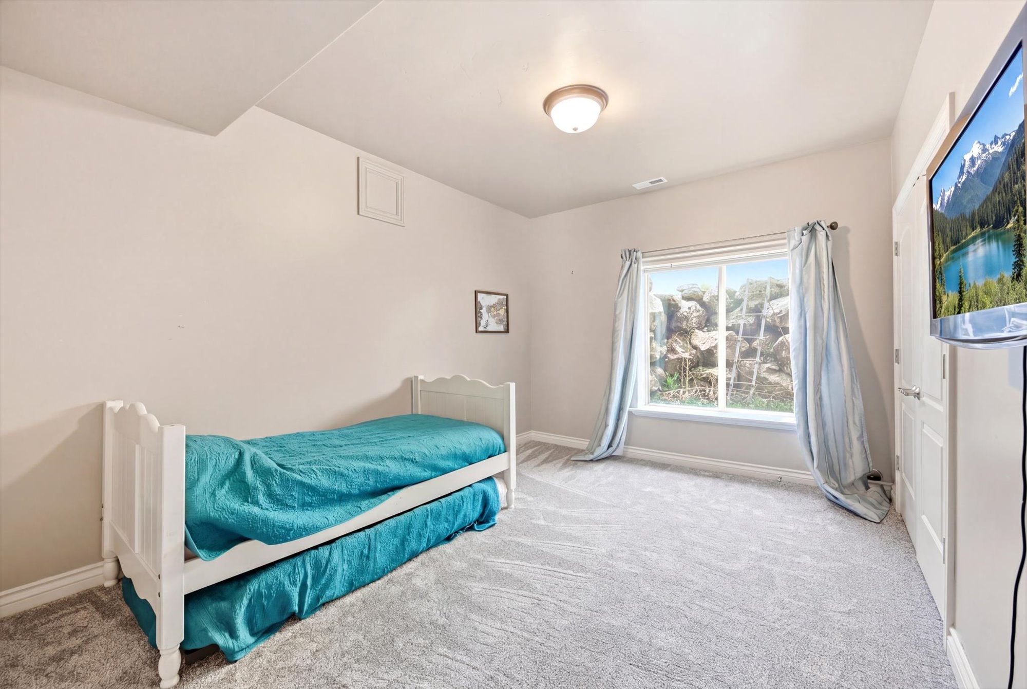 Carpeted room with a single window featuring light-colored curtains