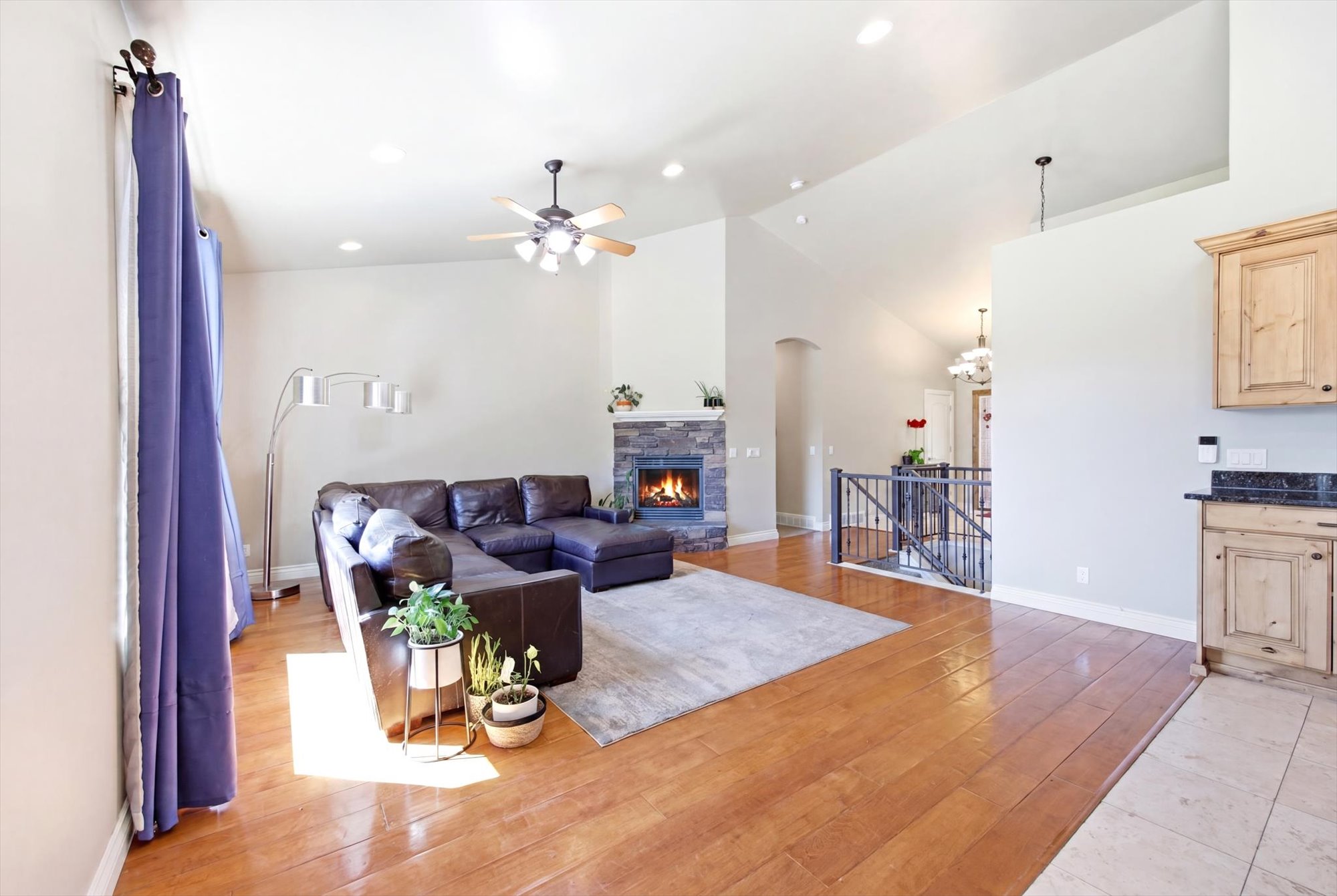 Spacious living area featuring wood-finish flooring, a stone-faced fireplace, vaulted ceilings, a ceiling fan, and recessed lighting