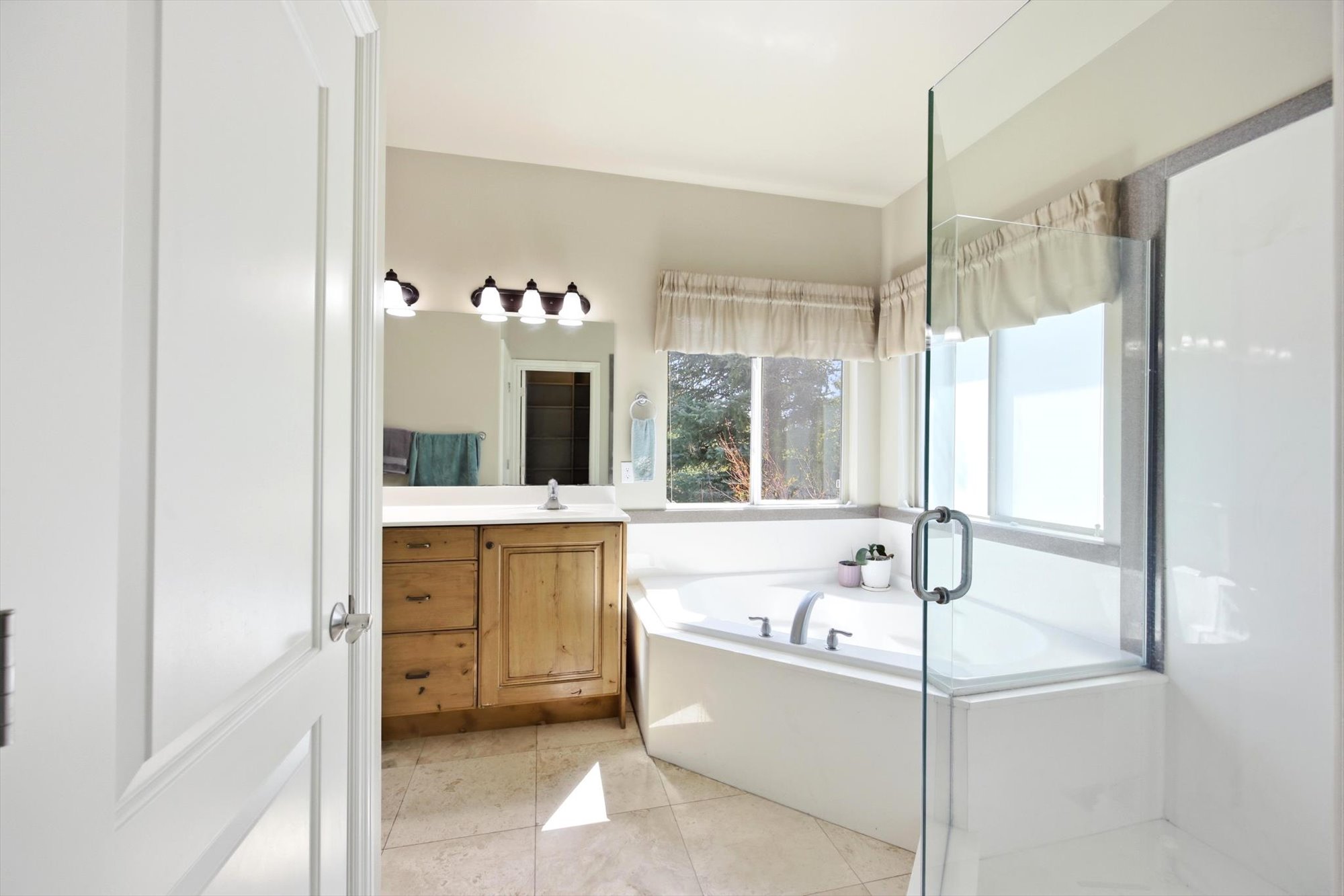 Bathroom featuring a built-in corner soaking tub, clear glass shower enclosure, wood-finish vanity with a white countertop, and tiled flooring